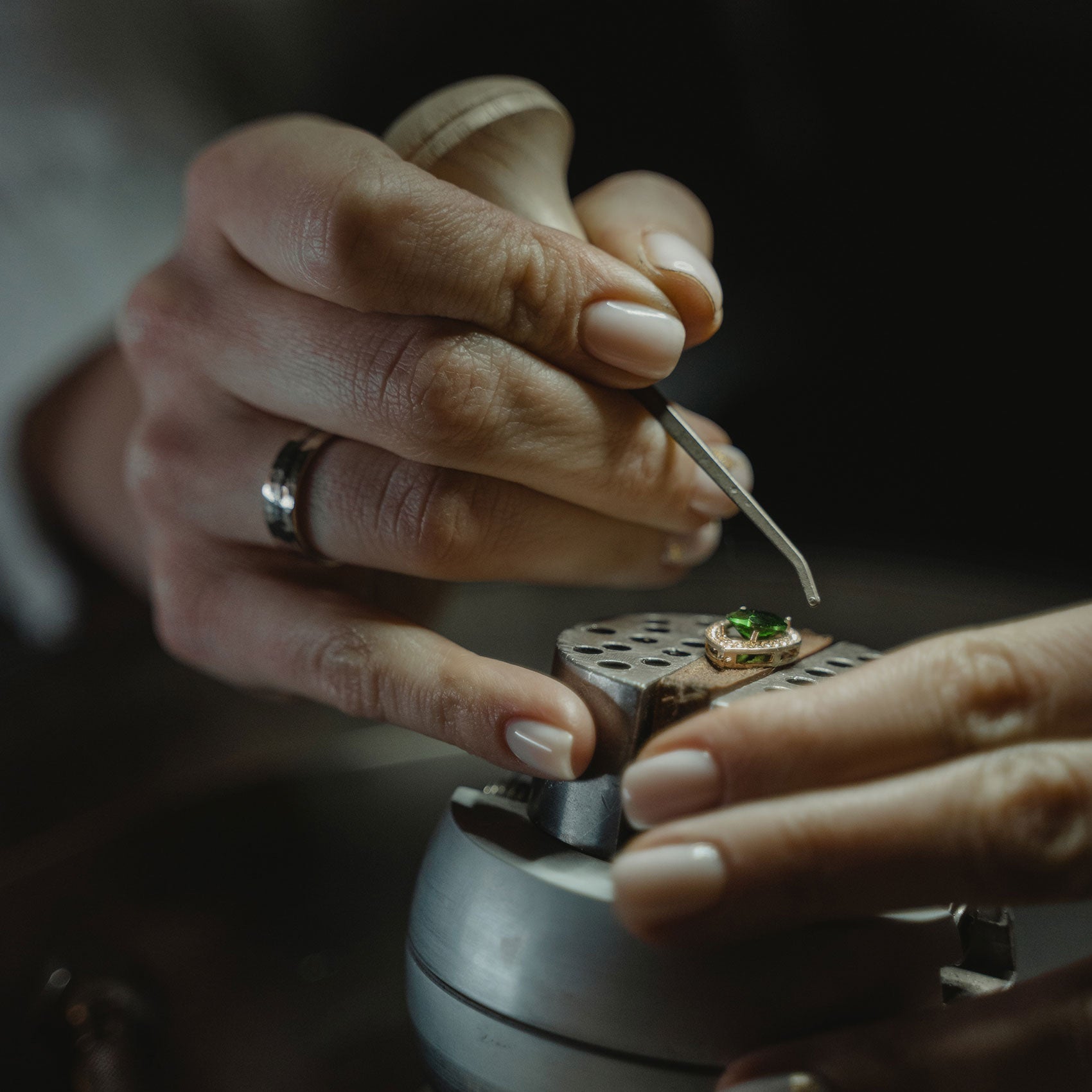 Gros plan d’un joaillier sertissant une émeraude poire sur un pendentif en or, reflet de maîtrise artisanale.