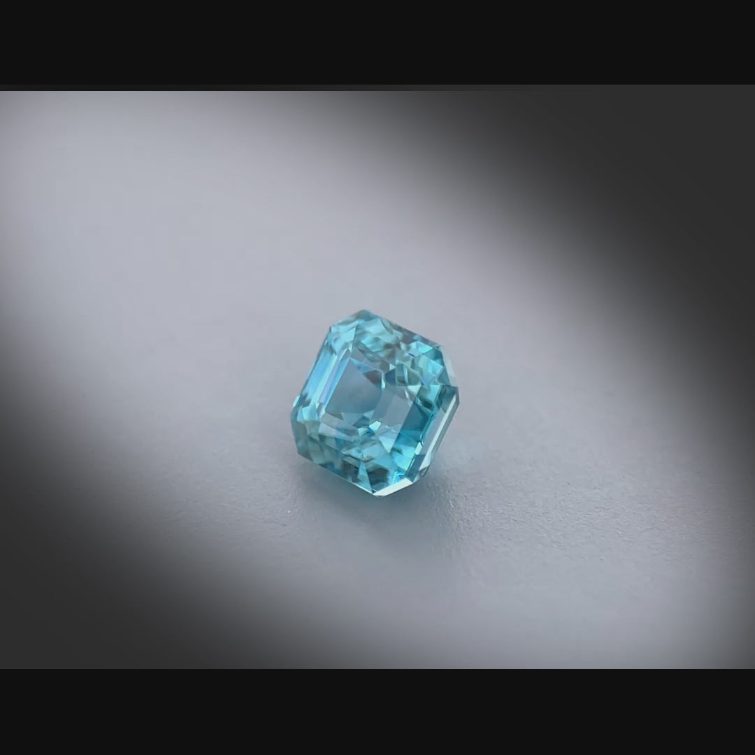 Vidéo d’un zircon bleu naturel carré à pans coupés de 1.41 ct, facetté, de couleur cyan-bleuté soutenu, originaire du Cambodge, tournant à 360 degrés sur fond gris clair