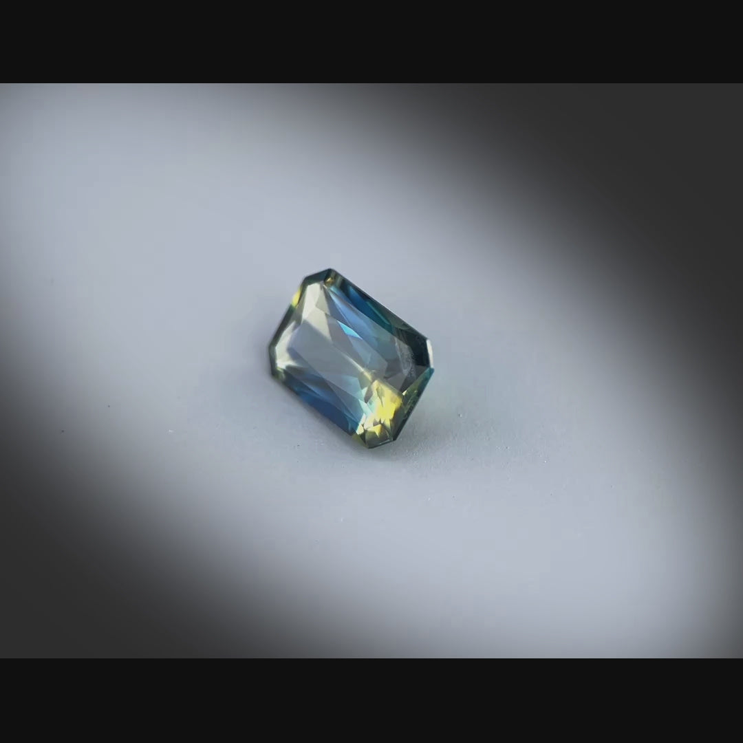 Vidéo montrant un saphir bicolore 1,68 ct de Madagascar, taille rectangle à pans coupés, facettes scintillantes sous différents angles.