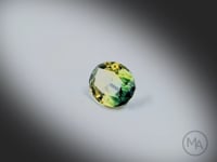 Vidéo d’un saphir bicolore naturel ovale facetté de 2.62 ct, certificat non chauffé, originaire d’Australie, aux couleurs vert bleuté et jaune, tournant sur un fond gris clair.