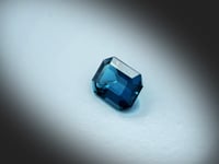 Vidéo d’une topaze bleue naturelle London Blue rectangle à pans coupés facettée de 2.64 ct, originaire du Brésil, de cyan-bleuté profond, rotation sur un fond gris clair.