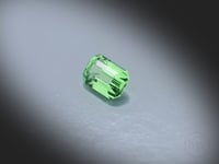 Vidéo d’un Grenat Tsavorite naturel rectangle à pans coupés facetté de 1.01 ct, originaire de Merelani en Tanzanie, de couleur vert prononcé, gemme rare tournant sur un fond gris clair.