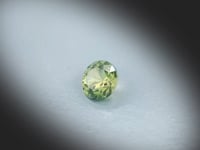 Saphir bicolore naturel de 1.50 ct, originaire d’Australie, rond et facetté, présentant des nuances jaunes et bleu-vert asymétriques, filmé en rotation sur fond gris clair.