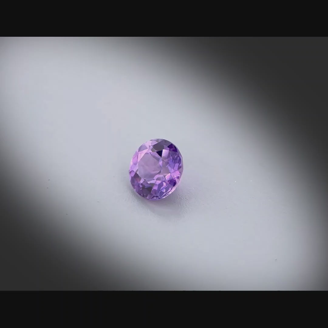 Vidéo d’un saphir violet-rosé naturel chauffé rond de 0.63 ct, chauffé, originaire de Madagascar, tournant à 360 degrés sur fond gris clair