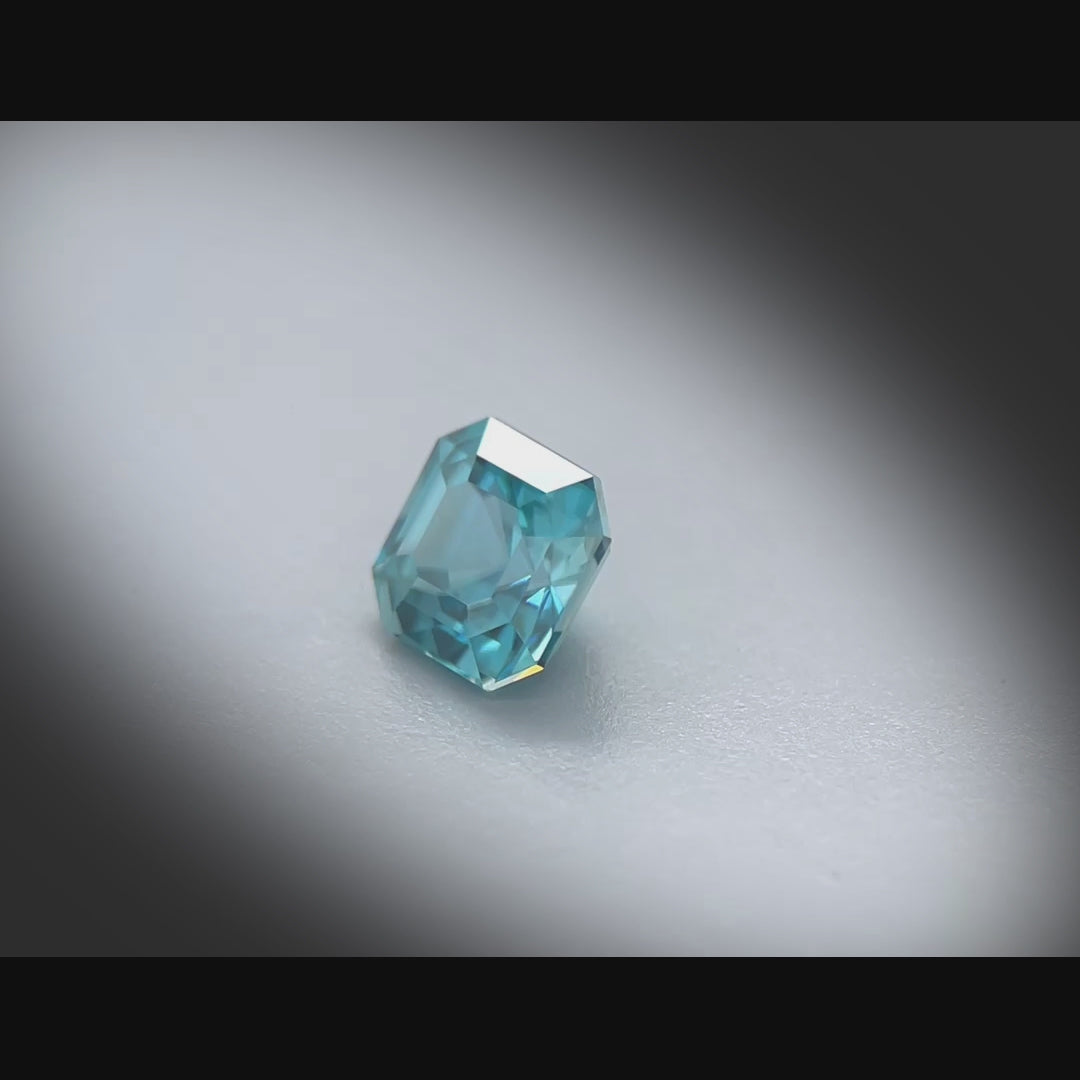 Vidéo d’un zircon bleu naturel carré à pans coupés de 1.43 ct, facetté, de couleur cyan-bleuté soutenu, originaire du Cambodge, tournant à 360 degrés sur fond gris clair
