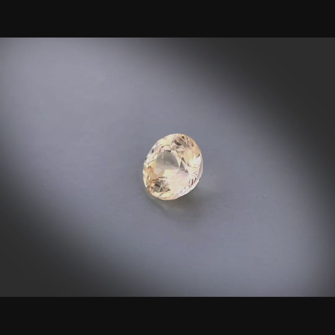 Vidéo d’un saphir pêche naturel non chauffé rond de 1.28 ct, originaire du Sri Lanka, de couleur brun-jaune légère, tournant à 360 degrés sur un fond gris clair
