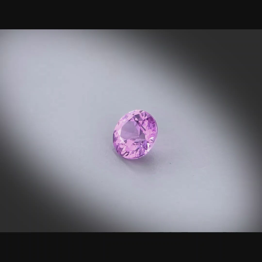 Vidéo d’un saphir rose-violet naturel rond de 0.64 ct, non chauffé, originaire de Madagascar, tournant à 360 degrés sur fond gris clair