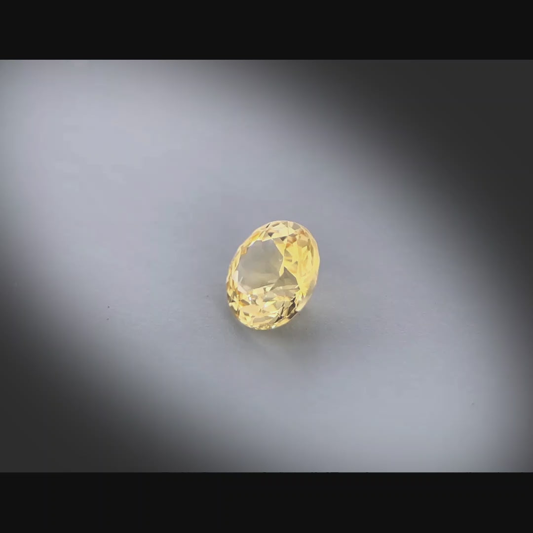 Vidéo d’un saphir jaune naturel non chauffé rond de 0.98 ct, originaire de Madagascar, de couleur jaune-doré soutenu, tournant à 360 degrés sur un fond gris clair