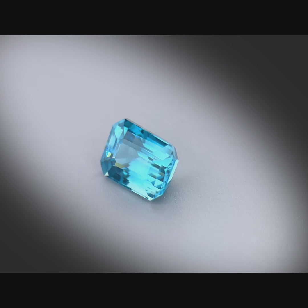 Vidéo d’un zircon bleu cyan naturel de 2.29ct, taillé en rectangle à pans coupés, tournant à 360° sur fond gris clair
