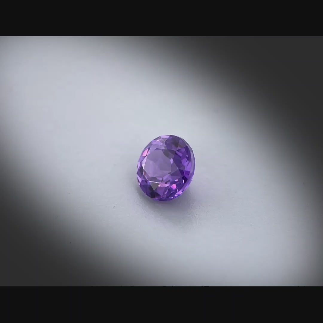 Vidéo d’un saphir violet naturel non chauffé rond de 0.91 ct, originaire du Sri Lanka, de couleur violet profond, tournant à 360 degrés sur un fond gris clair