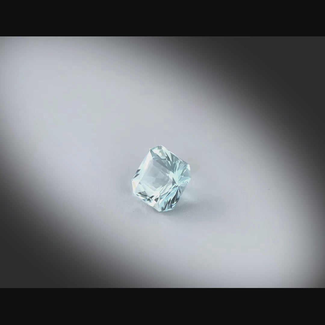 Vidéo d’une aigue-marine naturelle carrée à pans coupés de 1.11 ct, facettée, de couleur cyan-bleuté très léger, originaire de Madagascar, tournant à 360 degrés sur fond gris clair