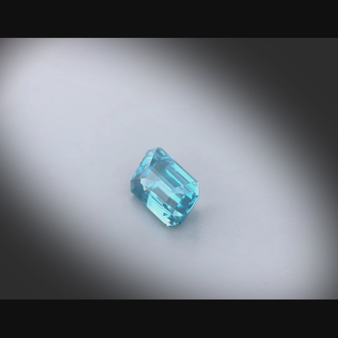 Vidéo d’un zircon bleu cyan naturel de 1.54 ct, taillé en rectangle à pans coupés, tournant à 360° sur fond gris clair