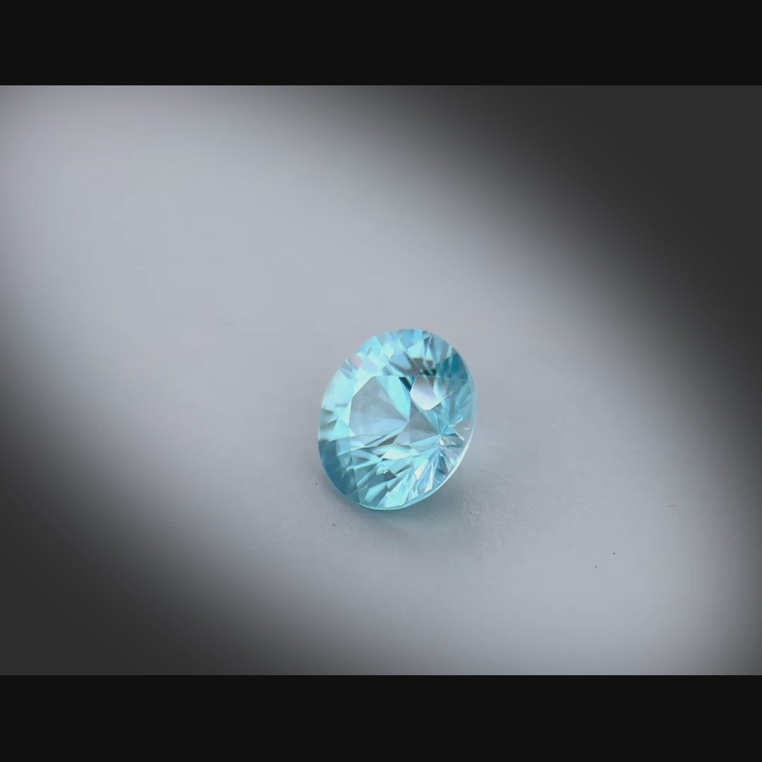 Vidéo d’un zircon bleu naturel rond de 1.46 ct, facetté, de couleur cyan-bleuté prononcé, originaire du Cambodge, tournant à 360 degrés sur fond gris clair