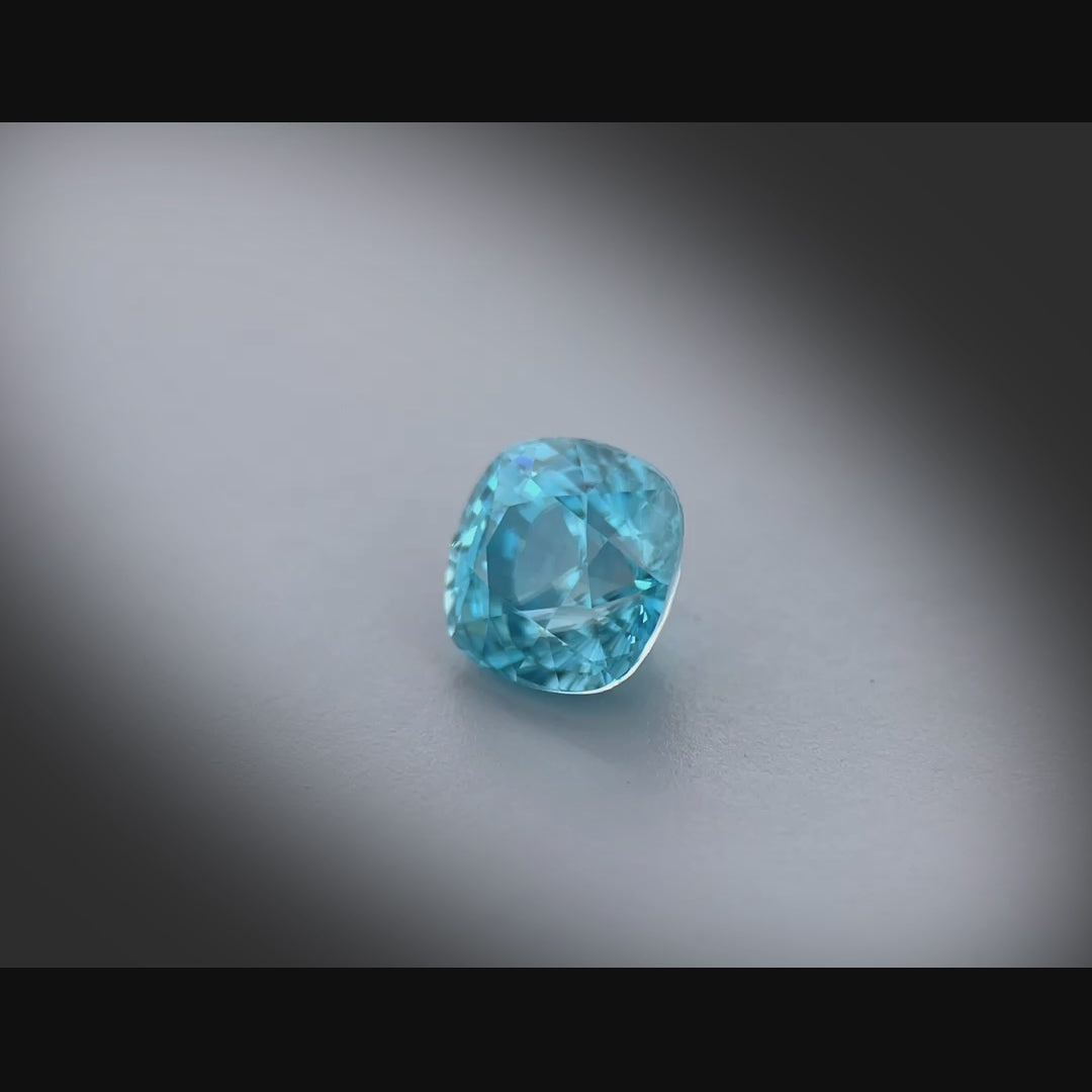 Vidéo d’un zircon naturel bleu coussin carré de 2.77ct, facetté, cyan bleuté soutenu, sans inclusion visible, tournant à 360 degrés sur fond gris clair.