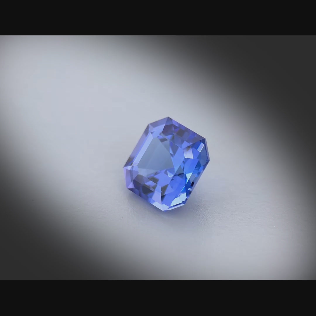 Vidéo d’une tanzanite naturelle de 2.45 ct, taillée en carré à pans coupés, bleu-violet soutenu, tournée à 360° sur fond gris clair.
