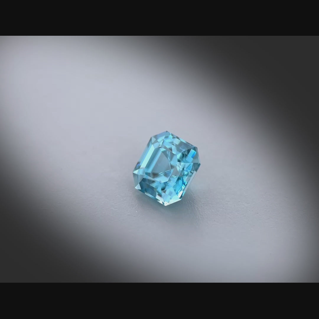 Vidéo d’un zircon bleu naturel carré à pans coupés de 1.49 ct, facetté, de couleur cyan-bleuté soutenu, très légèrement inclus, originaire du Cambodge, tournant à 360 degrés sur fond gris clair