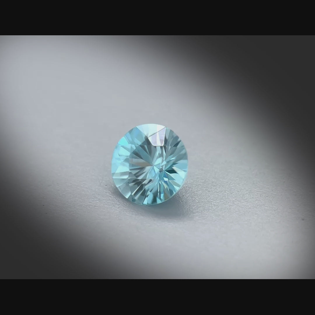 Vidéo d’un zircon bleu naturel rond de 1.26 ct, facetté, de couleur cyan-bleuté prononcé, originaire du Cambodge, tournant à 360 degrés sur fond gris clair