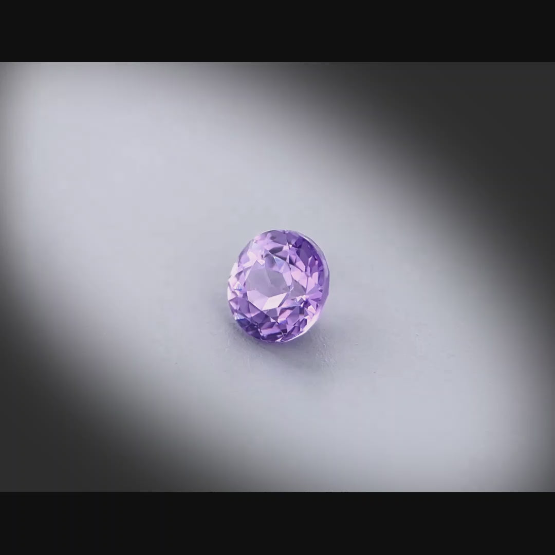 Vidéo d’un saphir violet-rosé naturel non chauffé rond de 0.87 ct, originaire de Madagascar, tournant à 360 degrés sur fond gris clair