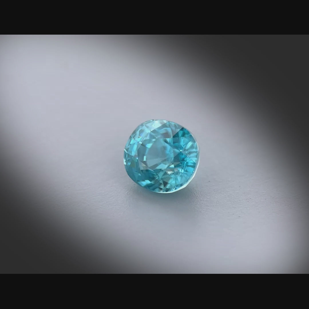 Vidéo d’un zircon naturel bleu ovale de 2.68ct, facetté, cyan bleuté soutenu, sans inclusion visible à la loupe 10x, tournant à 360 degrés sur fond gris clair.