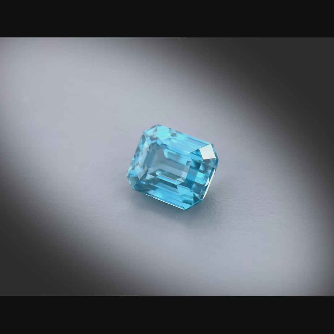 Vidéo d’un zircon bleu cyan naturel de 2.37 ct, taille rectangle à pans coupés, tournant à 360° sur fond gris clair