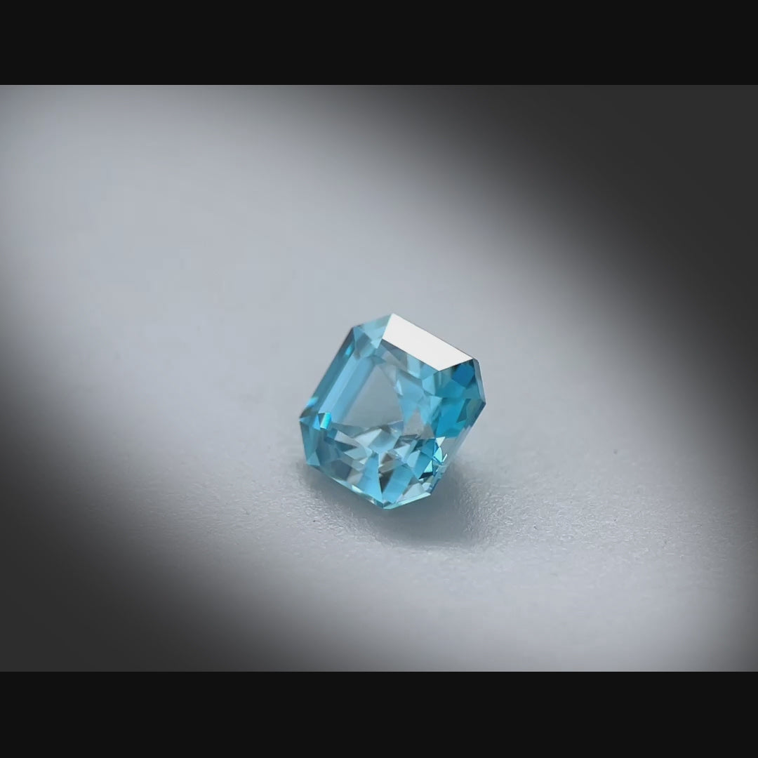 Vidéo d’un zircon bleu naturel carré à pans coupés de 1.37 ct, facetté, de couleur cyan-bleuté soutenu, originaire du Cambodge, tournant à 360 degrés sur fond gris clair