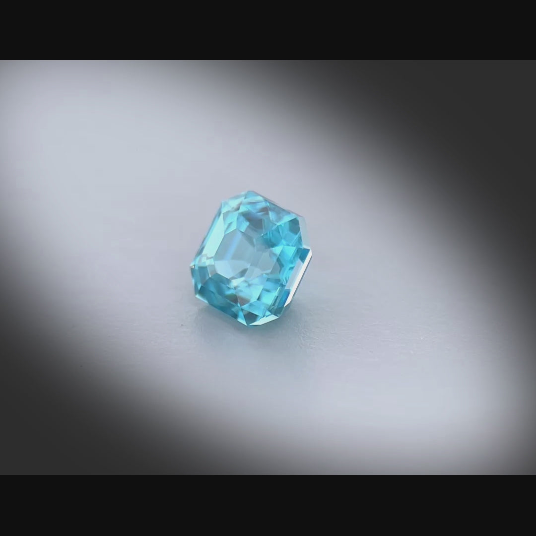 Vidéo d’un zircon bleu cyan naturel de 1.29 ct, facetté en carré à pans coupés, tournant à 360° sur fond gris clair