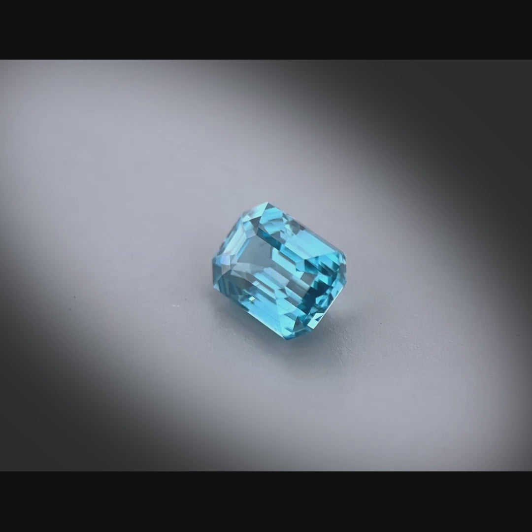 Vidéo d’un zircon bleu cyan naturel de 1.60 ct, facetté en rectangle à pans coupés, tournant à 360° sur fond gris clair