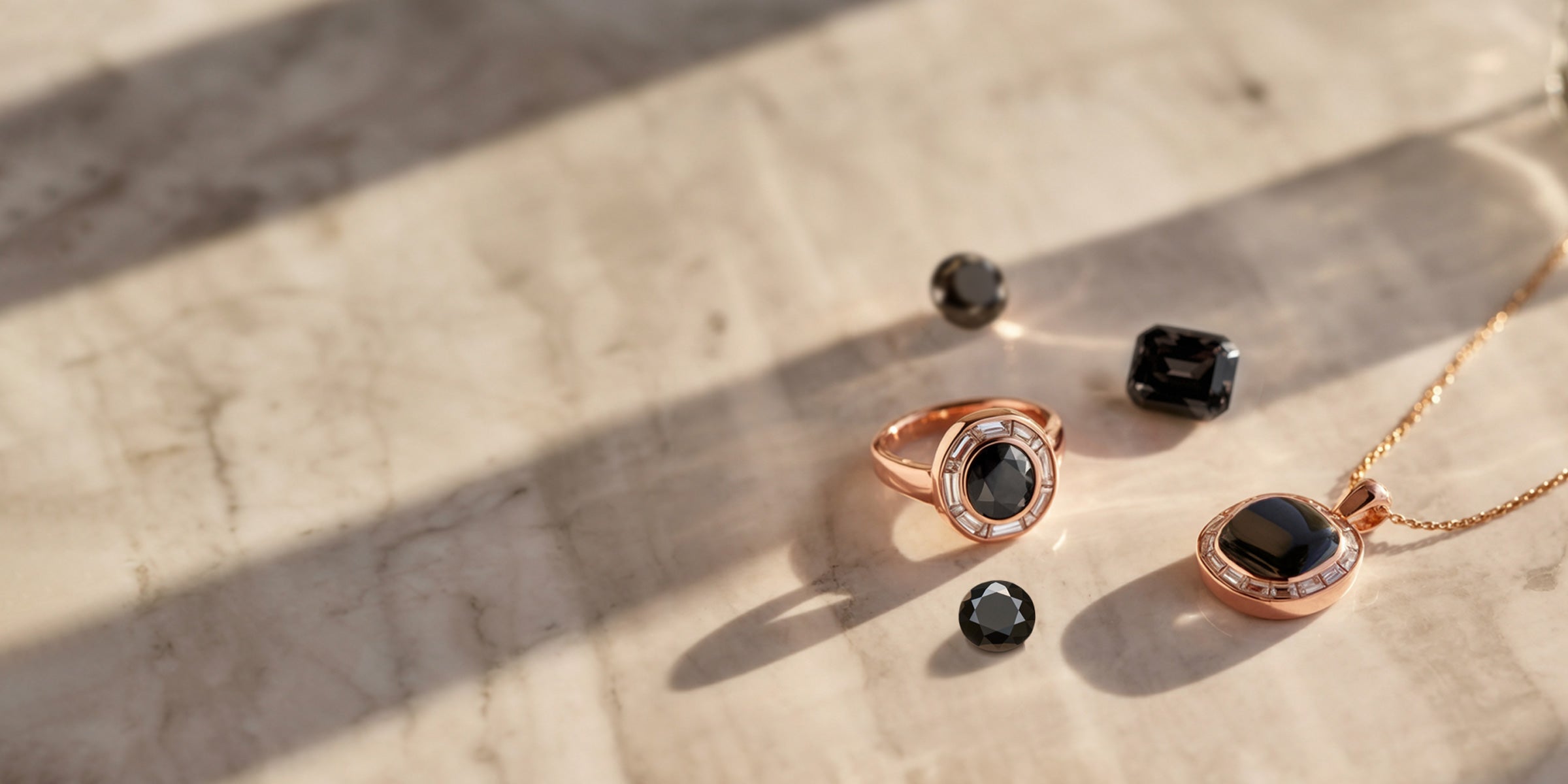 Composition élégante de bijoux en or rose avec pierres précieuses noires : bague en diamant noir, pendentif en onyx, spinelle et quartz fumé sur marbre crème.