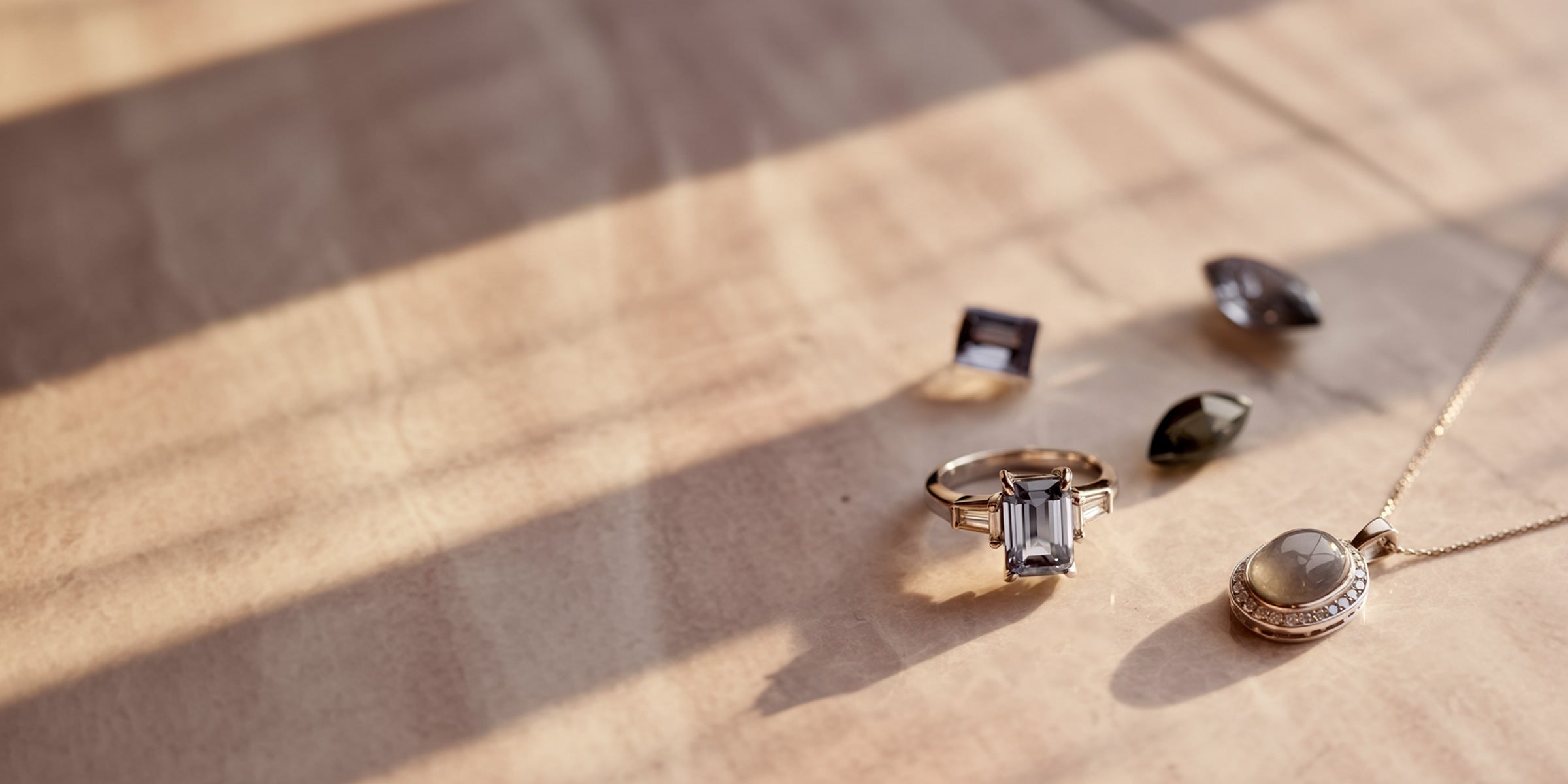 Bijoux de luxe en pierres fines grises, comprenant une bague spinelle rectangulaire et un pendentif en pierre de lune, élégamment posés sur marbre