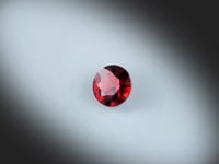 Grenat Rouge naturel de 1.50 ct, originaire de Madagascar, rond facetté, dévoilant une couleur rouge profonde au fil de sa rotation sur fond gris clair.