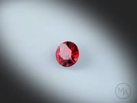 Grenat Rouge naturel de 1.12 ct, originaire de Madagascar, rond et facetté, arborant une couleur rouge profond, présenté en rotation sur un fond gris clair.