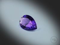 Améthyste naturelle de 3.88 ct, originaire de Zambie, taillée en poire et facettée, révélant une couleur violet-rosé intense, filmée en rotation sur fond gris clair.