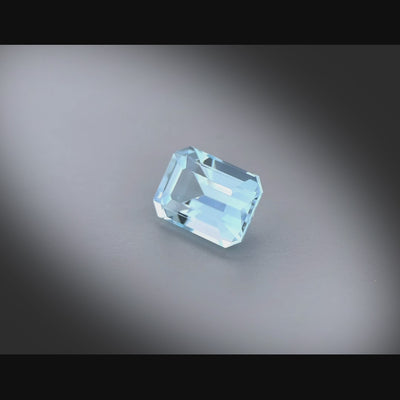 Vidéo d’une aigue-marine naturelle de Madagascar, taille rectangle à pans coupés facettée de 1.47 ct, de couleur cyan bleuté léger, tournant sur un fond gris clair.