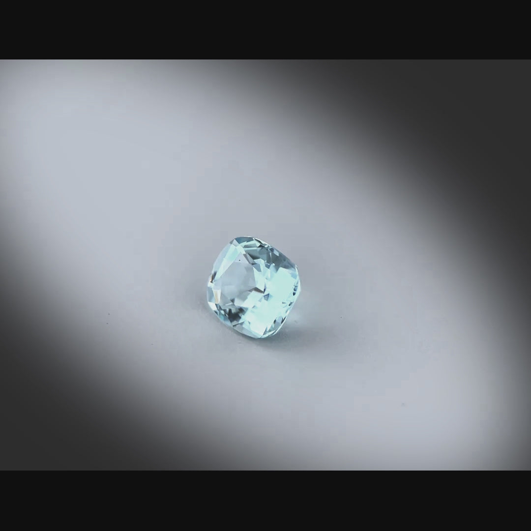 Vidéo d’une aigue-marine naturelle coussin rectangle facettée de 0.95 ct, originaire de Madagascar, de couleur cyan bleuté très léger, rotation sur un fond gris clair.