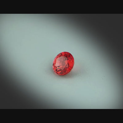 Vidéo d’un spinelle rouge naturel rond facetté de 0.72 ct, originaire de Mahenge en Tanzanie, de couleur rouge orangé intense, rotation sur un fond gris clair.